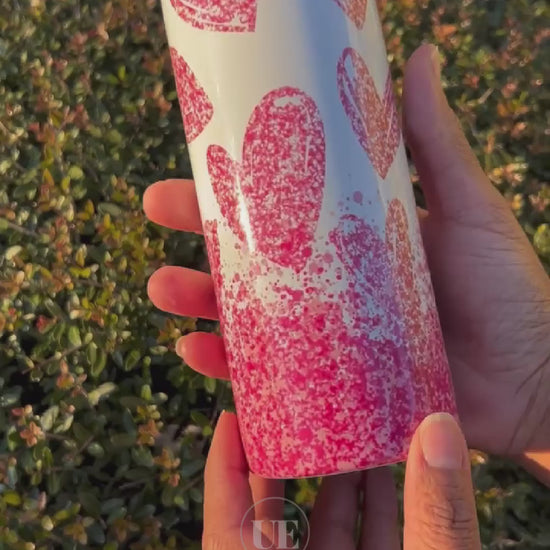 A video of a 20oz Stainless Steel skinny tumbler with falling pink hearts and a white background and includes a silicone bottom, leakproof top, metal straw and straw cleaner.