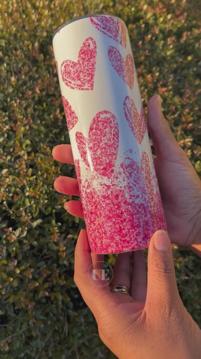 A video of a 20oz Stainless Steel skinny tumbler with falling pink hearts and a white background and includes a silicone bottom, leakproof top, metal straw and straw cleaner.